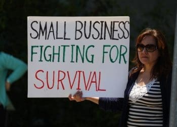 A small business owner with a sign explaining her troubles during the Covid-19 pandemic. Photo by Gene Gallin/Unsplash